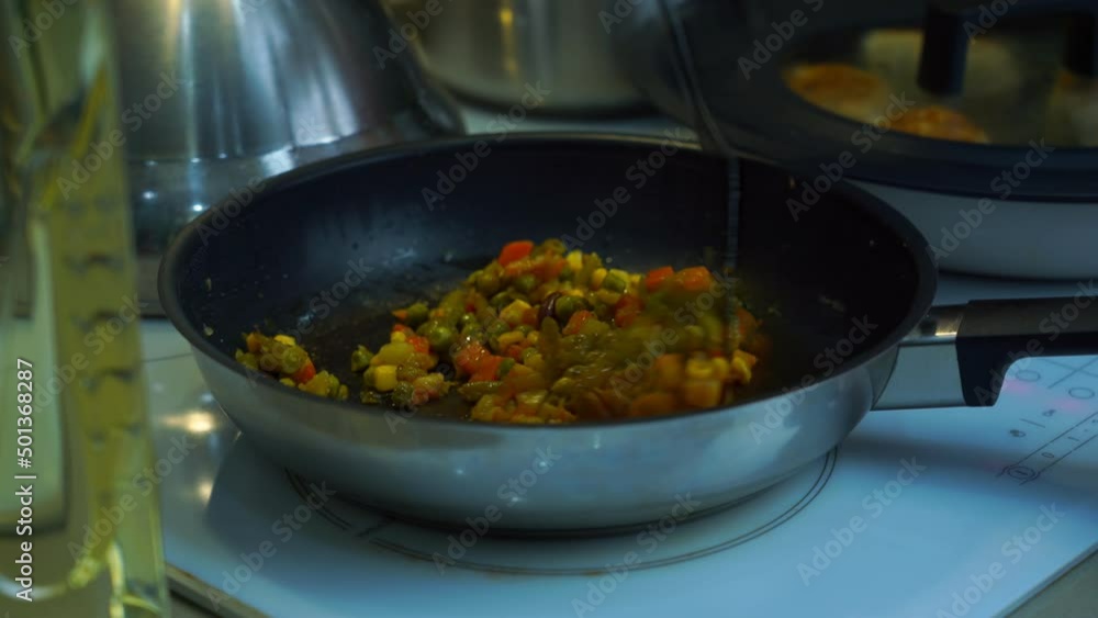 Female hand with spatula mixing vegetables in frying pan standing on induction stove. Healthy and vegetarian eating concept. Female hand with spatula mixing vegetables in frying pan standing on induction stove. Healthy and vegetarian eating concept.