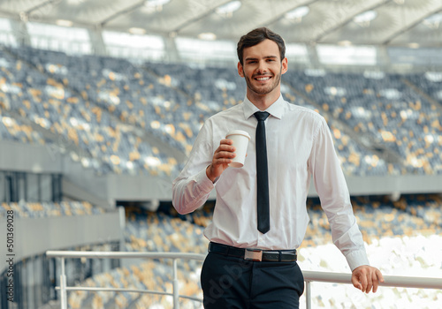 Obraz na plátně Smiling man entrepreneur drinking coffee while standing on observation deck of t