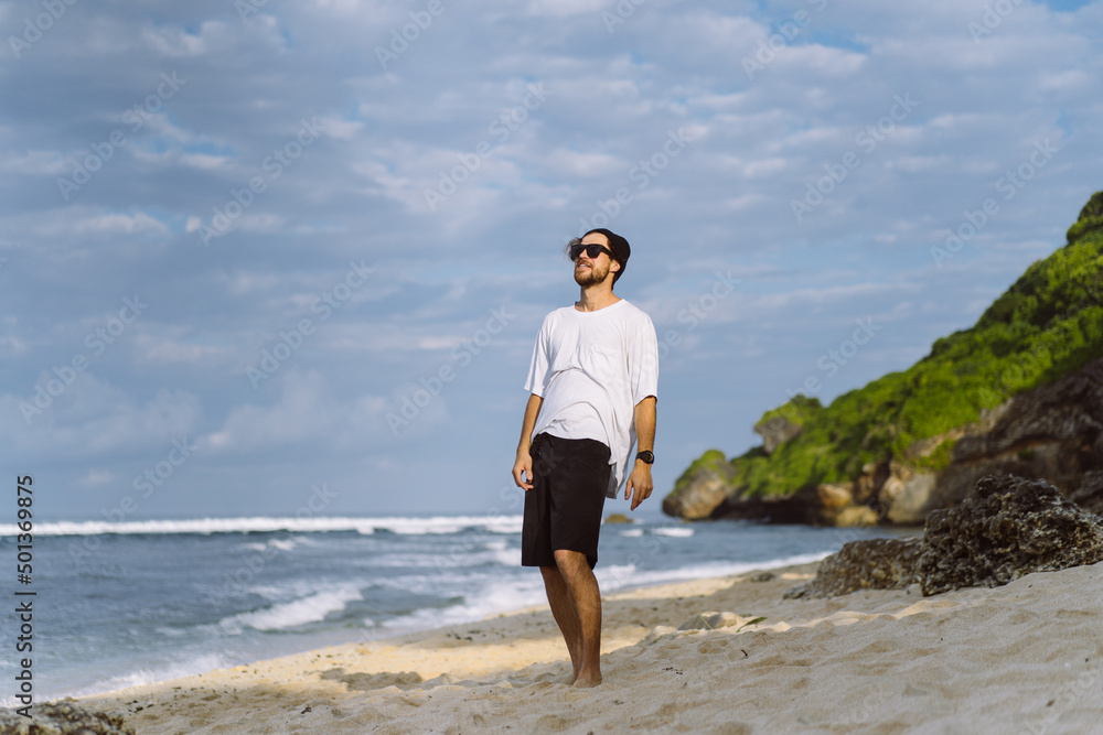 Young handsome man with a charming smile in sunglasses on the beach.