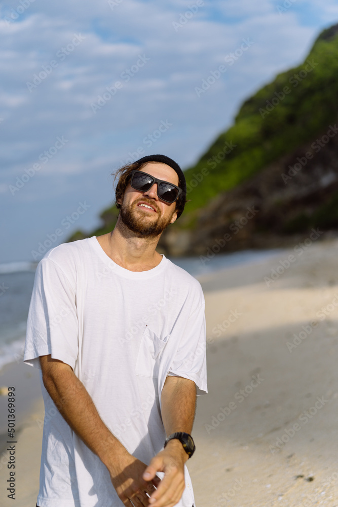 Young handsome man with a charming smile in sunglasses on the beach.