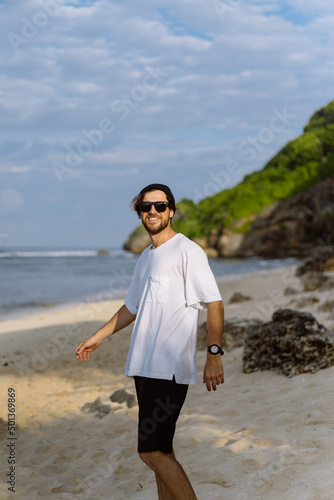 Young handsome man with a charming smile in sunglasses on the beach. © Yuliya Kirayonak