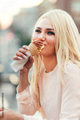 Emotional  woman  blonde  with two ice creams posing against the backdrop of the city. Warm evening day. In the background there are lights from cars.