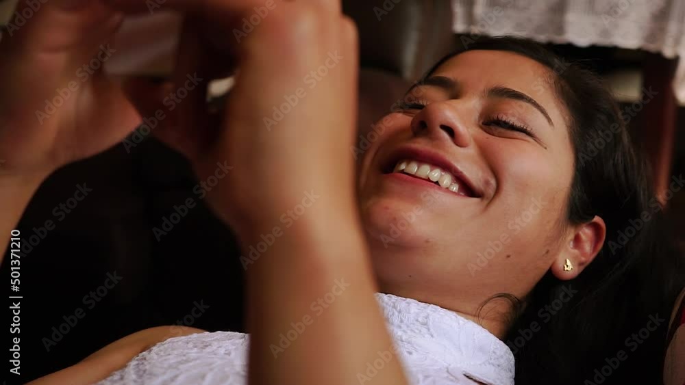 Mujer viendo su celular echada en sillón. Concepto de hogar y descanso.