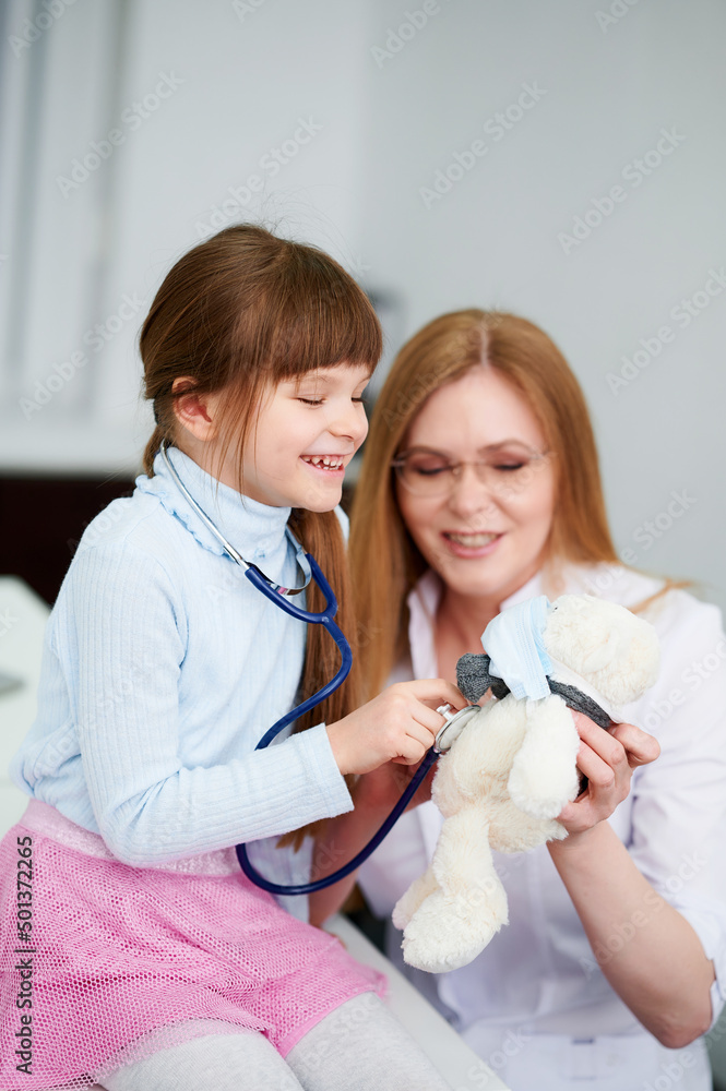 Caucasian female doctor with patient little girl examining by stethoscope bear toy in office Caucasian female doctor with patient little girl examining by stethoscope bear toy in office