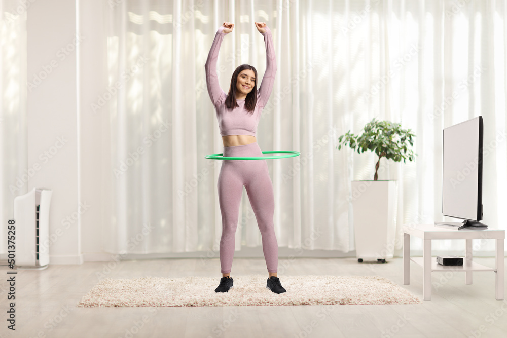 Full length portrait of a fit woman in sportswear exercising with a hula hoop in a room Full length portrait of a fit woman in sportswear exercising with a hula hoop in a room