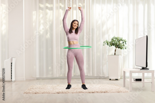 Full length portrait of a fit woman in sportswear exercising with a hula hoop in a room