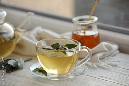 Foto Cup of sage tea and green leaves on white wooden windowsill