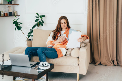 Concentrated young business woman working at home with paperwork and computer.