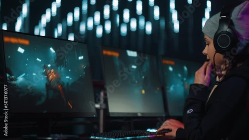 Excited participant female gamer plays 3D shooter video game on a tournament. On a screen  hero characters running and killing zombies.