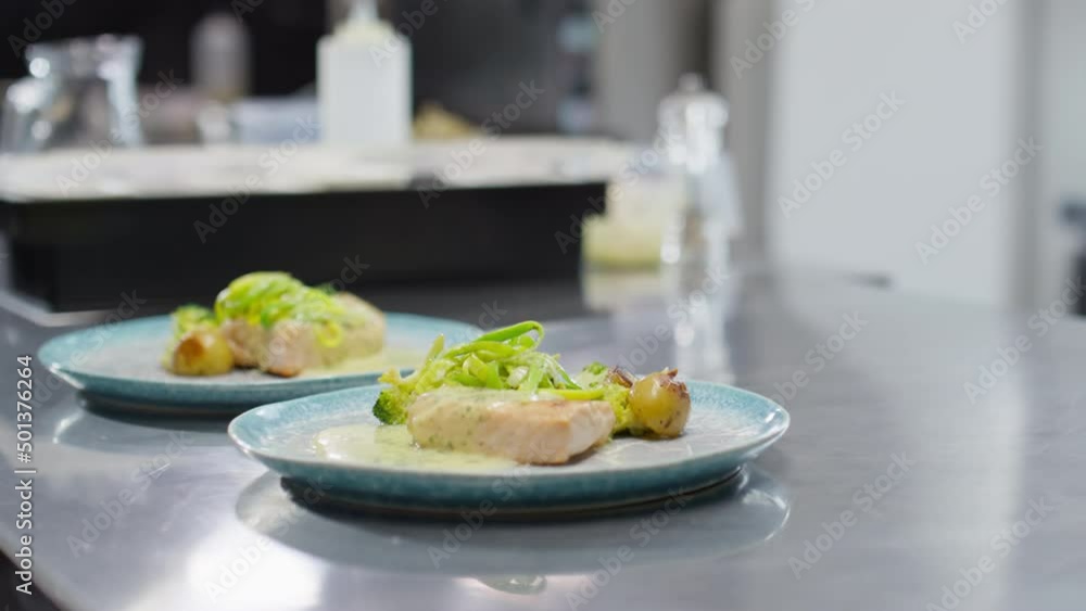 Cropped shot of unrecognizable male chef moving two plates with served dishes on metal table while giving food orders in restaurant kitchen Cropped shot of unrecognizable male chef moving two plates with served dishes on metal table while giving food orders in restaurant kitchen
