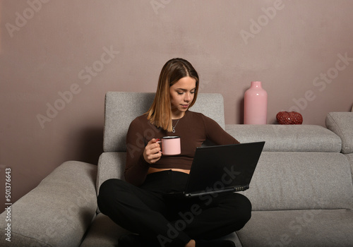 bellissima ragazza sorridente che lavora al computer bevendo una bevanda in una tazza rosa photo