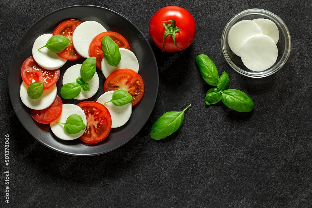Caprese, Italian antipasto appetizer, with ingredients for cooking - tomato, mozzarella and basil, on dark background, top view..
