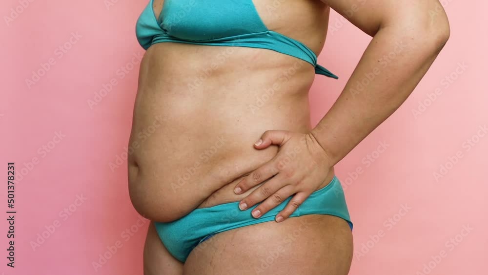 Closeup fat overweight woman morphing from fat to losing weight in blue swimsuit. Corpulent female posing at camera. Adipose and visceral fat. Pink isolated background. Before and after lose weight Closeup fat overweight woman morphing from fat to losing weight in blue swimsuit. Corpulent female posing at camera. Adipose and visceral fat. Pink isolated background. Before and after lose weight