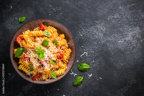 Italian pasta alla arrabiata with basil and parmesan on dark table. Fusilli pasta with tomato sauce. Top view, close up. photo