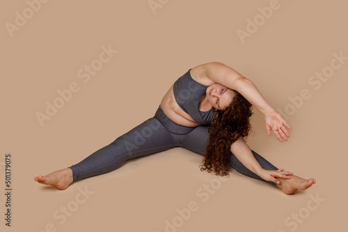 Concentrate curly haired, corpulency barefoot woman doing sports gymnastics incline with arms to right. Wearing sportswear. Body positive and self acceptance, diversity body. Weight loss. Isolated