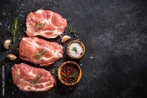 Raw meat. Fresh meat steaks with herbs and spices at black stone background. Close up image. Top view with space for design.