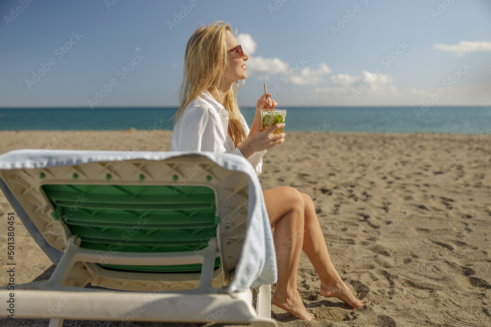 Side view of happy woman enjoying mohito cocktail and smiling away on empty beach Side view of happy woman enjoying mohito cocktail and smiling away on empty beach
