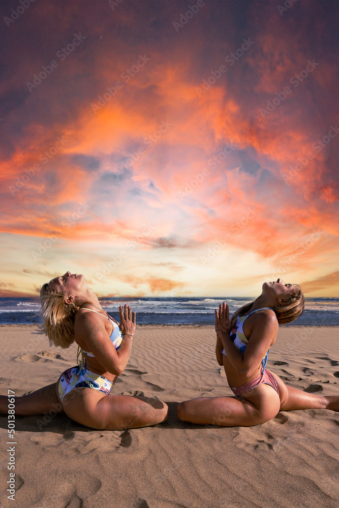 Two young women doing yoga at sunset at the beach