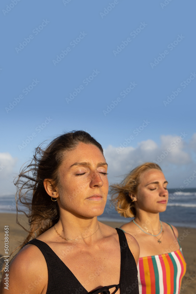 Portrait of two women meditating with their eyes closed on the beach