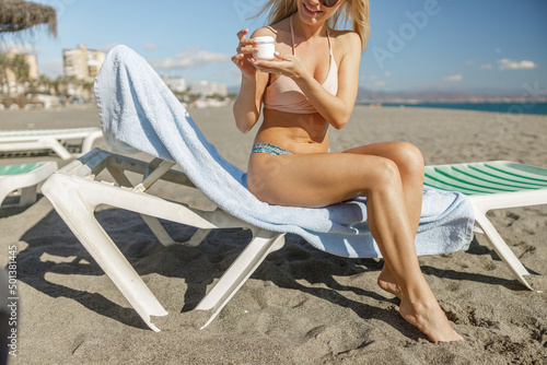 Woman in bikini using body lotion in jar while sunbathing on beach
