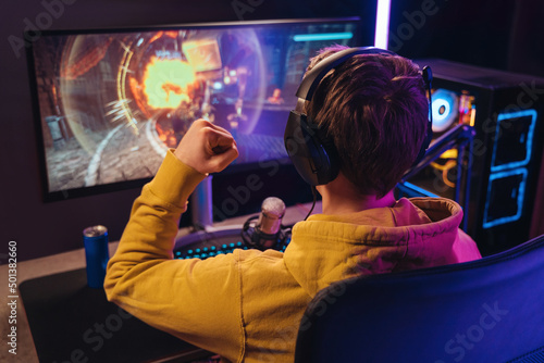 Fotografía Back view of streamer young man rejoices his victory in esport shooter game tournament, making winner hand gesture
