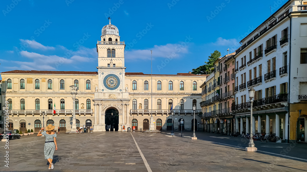 Tourist woman with scenic view on the astronomical clock from empty Piazza dei Signori in Padua, Veneto, Italy, Europe. Column of winged lion statue of Saint Mark background Astronomical Clock. Padova
