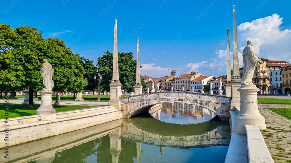 Man in a dress and hat sitting on bridge of Prato della Valle, square in the city of Padua, Veneto, Italy, Europe. Isola Memmia surrounded by canal bordered by two rings of statues. Reflection water