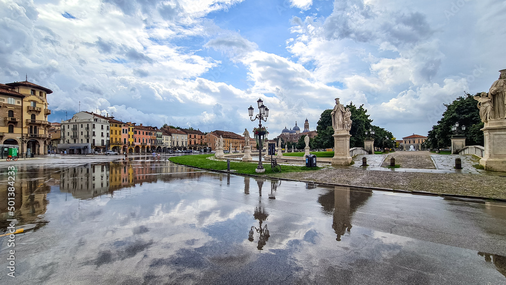 Naklejka premium Scenic view after strong rain on Prato della Valle, Abbey of Santa Giustina, square in city of Padua, Veneto, Italy, Europe. Rain storm and black clouds in sky. Water on street creates reflection