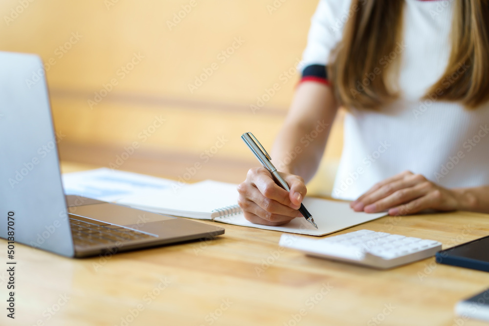 Close up image of a woman writing and taking note on notebook with laptop in office. Close up image of a woman writing and taking note on notebook with laptop in office.