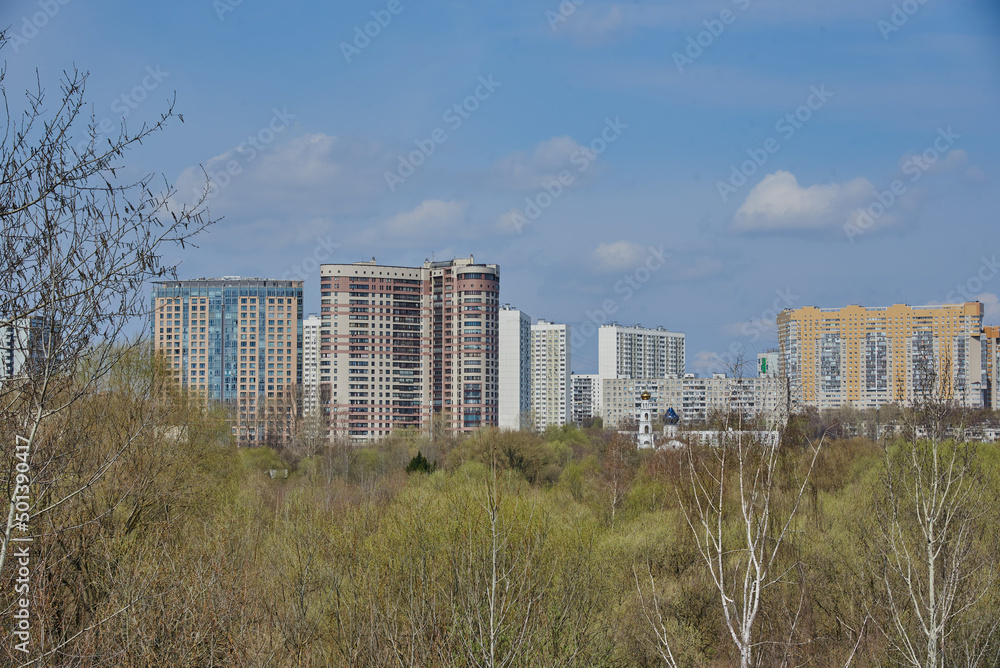 An urban residential area rises above a green park against a blue sky. An urban residential area rises above a green park against a blue sky.