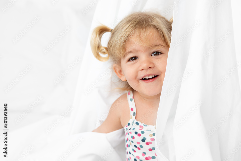 Happy toddler girl playing peekaboo behind white sheet Happy toddler girl playing peekaboo behind white sheet