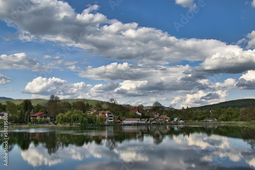 Scenic view of the houses and hills covered by forests under the cloudy sky reflecting in the water photo