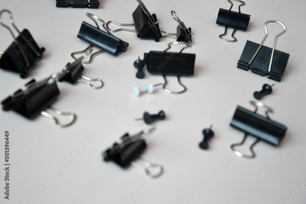 Black push pins and document clips and buttons scattered on a white background. Office tools. Black push pins and document clips and buttons scattered on a white background. Office tools.