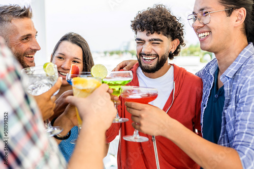 Group of happy multiracial best friends having fun together while enjoying drinks in summer party at rooftop beach bar. Friendship and celebration concept.