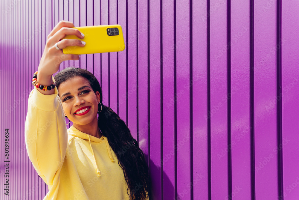 Happy girl taking a selfie portrait with her yellow smartphone on a ...
