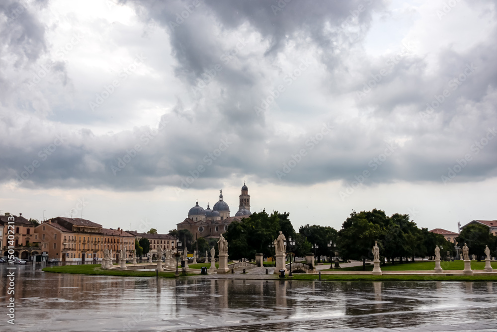 Scenic view after strong rain on Prato della Valle, Abbey of Santa Giustina, square in city of Padua, Veneto, Italy, Europe. Rain storm, black clouds in sky. Isola Memmia surrounded by canal, statues