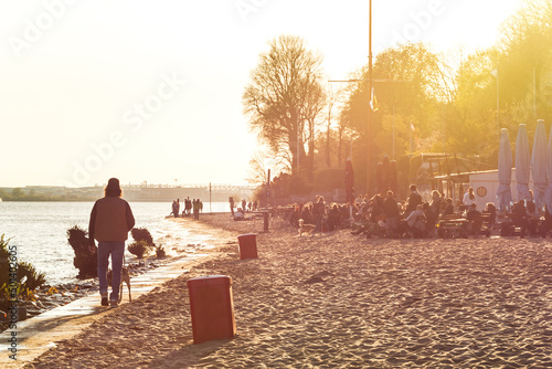 People relaxing at the beach at the Elbe River in Hamburg during colorful sunset