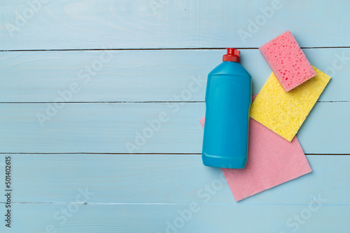 Bottle with dishwashing detergent and sponges on wooden background, top view