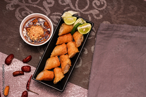 Fried spring rolls in a black plate served with tamarind dipping sauce on the table with black and gold placemats.