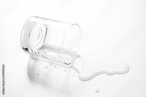.a glass of water spilled on a white table- Image