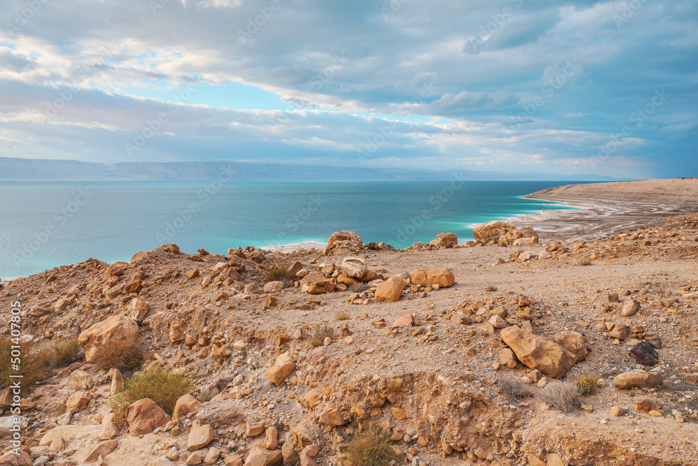 Dead sea shore at Jordan side, dry sand and rocks beach, sun shines on beautiful azure water surface