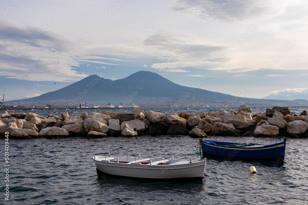 Two fishermen boats floating in the harbor of Naples, Campania, Italy, Europe. Panoramic view on volcano Mount Vesuvius. Ferries in the port. Clouds are accumulating around the mountains. Sea view