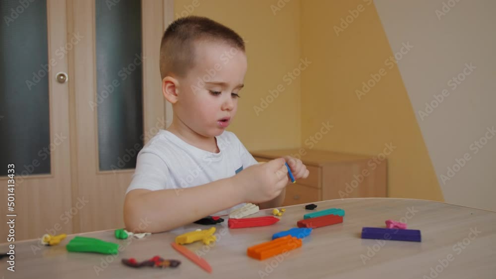 Little year boy playing molding colorful modeling clay, making toys sculpting playdough on table at home. Adorable child sculpts from plasticine Little year boy playing molding colorful modeling clay, making toys sculpting playdough on table at home. Adorable child sculpts from plasticine
