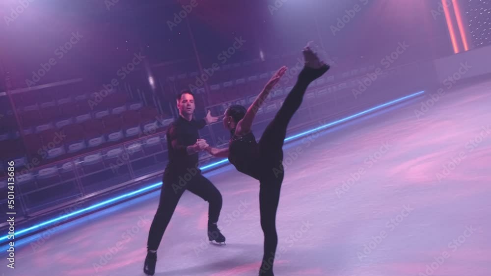 Figure skaters pair on ice rink in neon light skating by camera,man