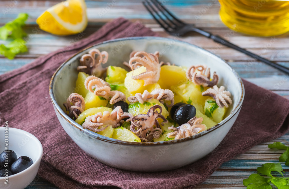Potato salad with small octopuses and olives in a gray bowl on a wooden background. Recipes for potato salads. Potato salad with small octopuses and olives in a gray bowl on a wooden background. Recipes for potato salads.