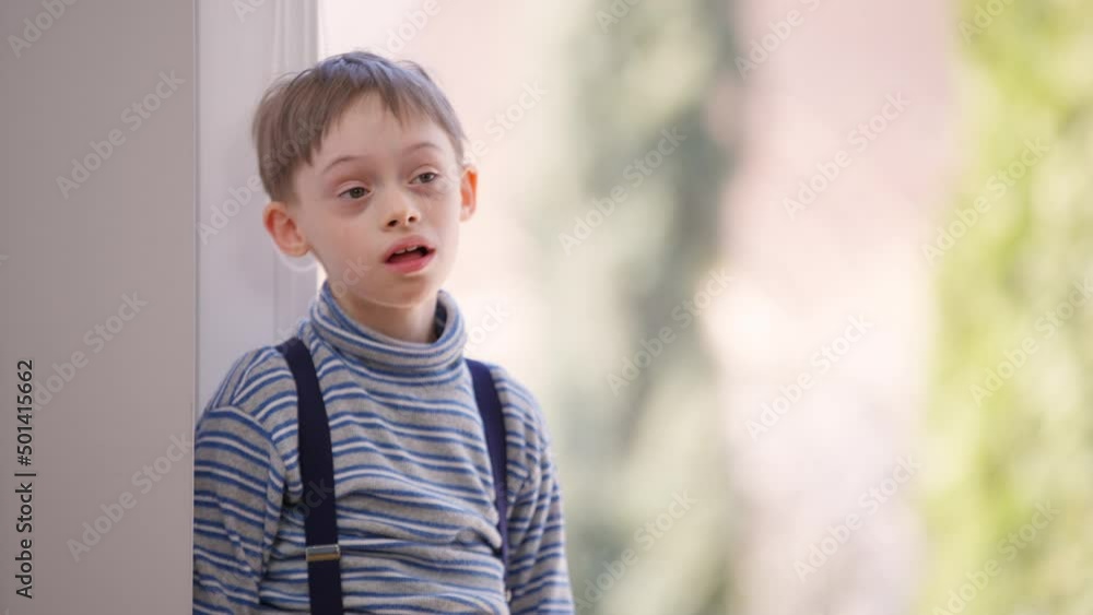 Portrait of distracted thoughtful autistic boy standing indoors looking away. Caucasian child with birth anomaly mental illness at glass door at home. Autism lifestyle concept Portrait of distracted thoughtful autistic boy standing indoors looking away. Caucasian child with birth anomaly mental illness at glass door at home. Autism lifestyle concept