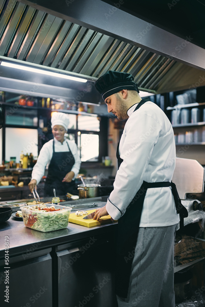 Male chef chopping food while working in kitchen at restaurant.