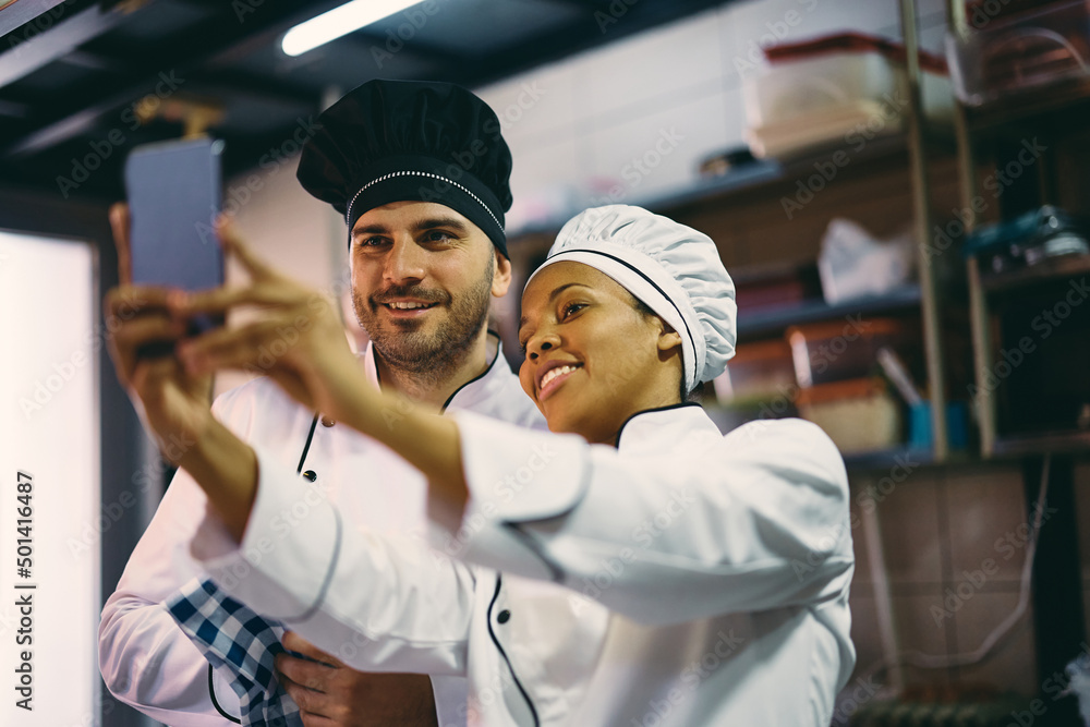 Fototapeta premium Happy cooks taking selfie while working at restaurant kitchen.