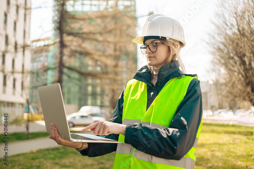 Industrial engineer woman in working uniform connected with PC laptop standing at the construction site. 