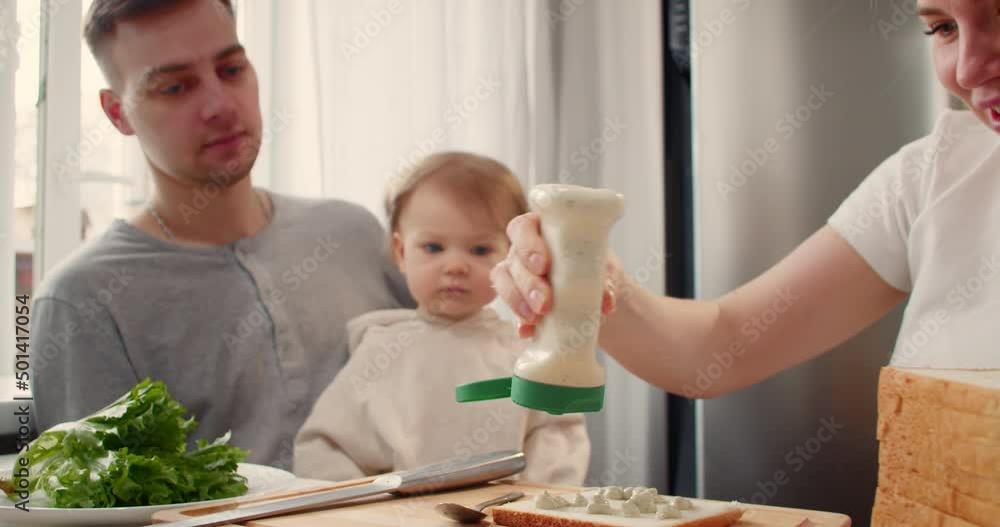 Mom making a sandwich with salad, ham and cheese for husbend and little doughter. American cuisine. Fast food. Cooking Mom making a sandwich with salad, ham and cheese for husbend and little doughter. American cuisine. Fast food. Cooking